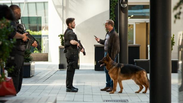 Ein Mann mit Hund spricht mit einem bewaffneten Polizisten, während weitere Polizisten im Hintergrund stehen.