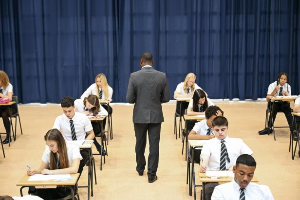 Exam supervisor walking between desks during exam, rear view