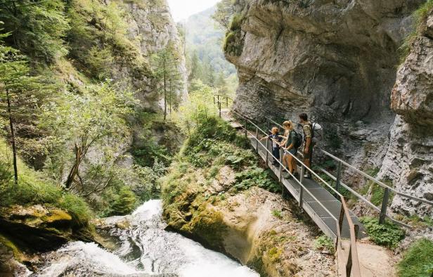 Menschen gehen über eine Brücke, die über einen Wasserfall in den Bergen führt.