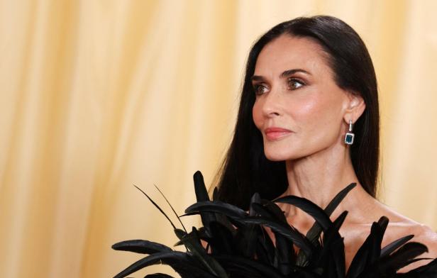 Demi Moore mit dunklen Federn und smaragdgrünen Ohrringen blickt zur Seite.