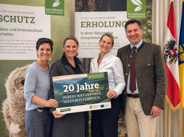 Vier Personen halten ein Schild mit der Aufschrift „20 Jahre Verein Naturparke Niederösterreich“ bei einer Jubiläumsveranstaltung vor Informationsplakaten und Landesflaggen.