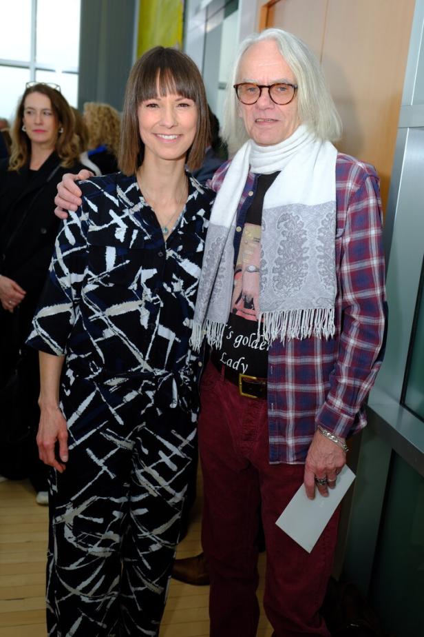 Zwei Personen posieren: Eine Frau im gemusterten Jumpsuit und ein Mann mit Schal und kariertem Hemd.