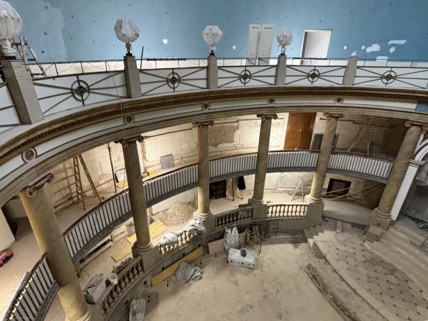 Großer, runder Saal mit zwei Etagen, Säulen, Balustraden und sichtbaren Renovierungsarbeiten sowie Baumaterialien.