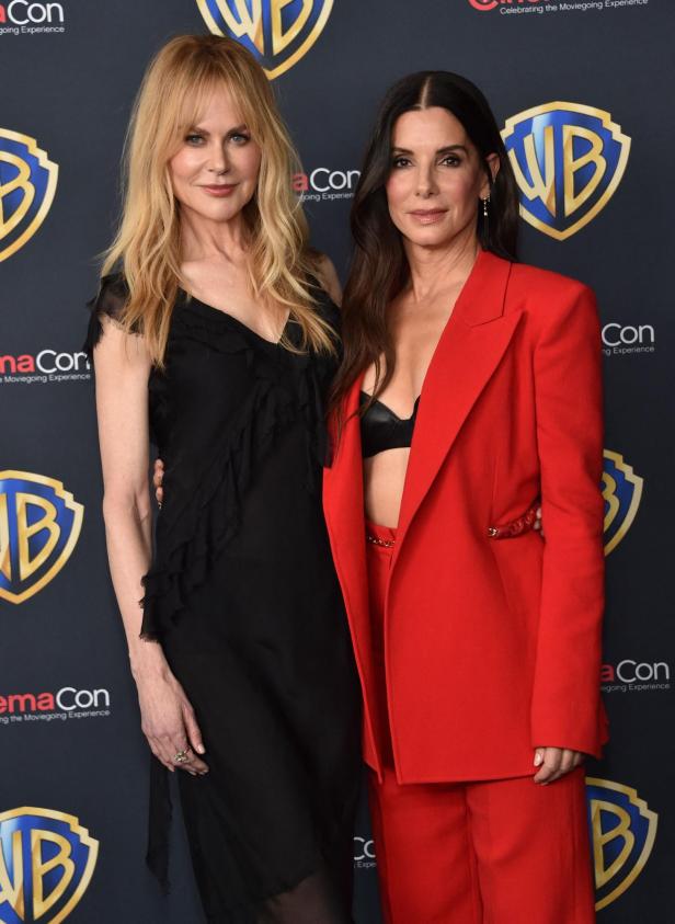 Nicole Kidman und Sandra Bullock posieren vor einem Warner Bros. Logo.