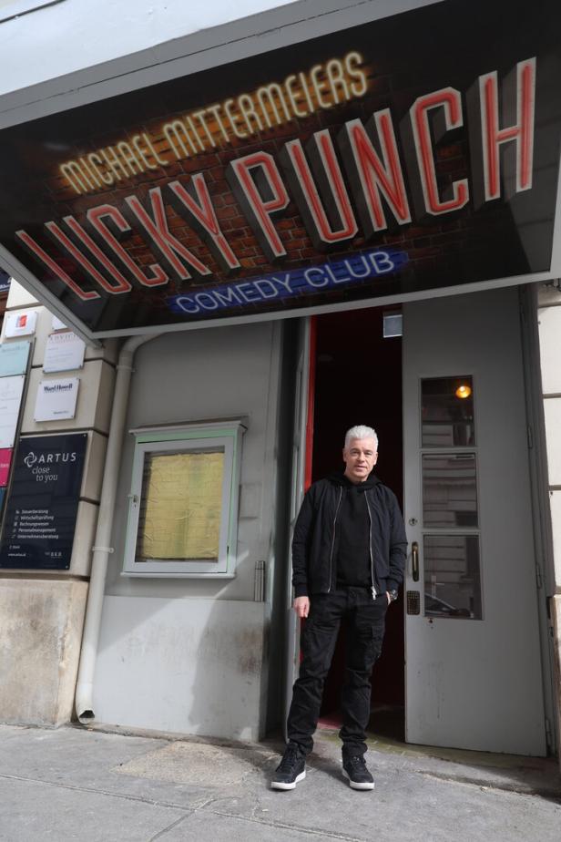 Michael Mittermeier steht vor dem Eingang eines Comedy Clubs mit dem Schriftzug „Lucky Punch“ über der Tür.