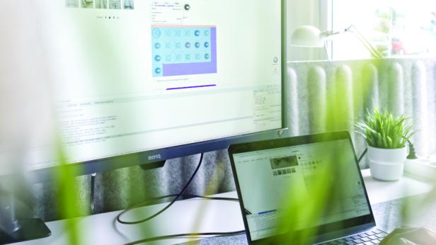 Eine Person sitzt an einem Schreibtisch mit einem Laptop und einem Monitor.