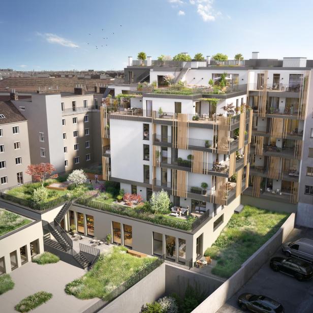 Modernes Wohngebäude mit mehreren Balkonen, begrünten Dachterrassen und Gartenflächen, umgeben von weiteren Häusern und geparkten Autos.