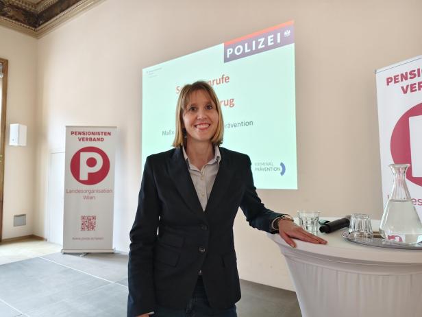 Eine Frau im Anzug steht lächelnd an einem Stehtisch bei einer Veranstaltung der Polizei und des Pensionistenverbands.