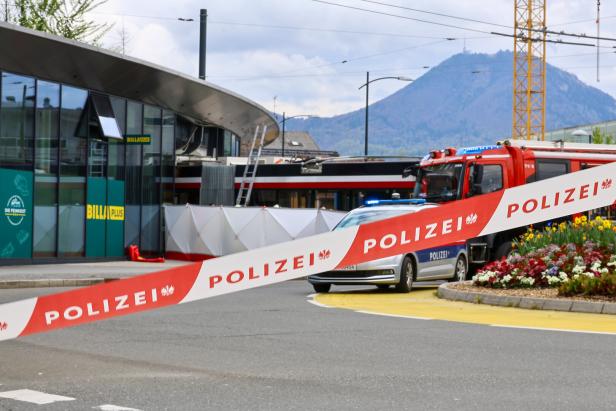 Absperrband der Polizei vor einem Supermarkt, dahinter Einsatzfahrzeuge und ein abgesperrter Bereich mit Sichtschutz.