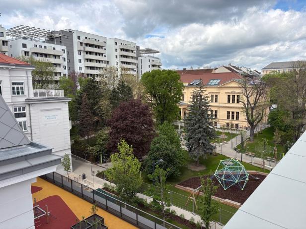 Blick auf einen Park mit Spielplatz, umgeben von Gebäuden, darunter der Karl Ludwig Pavillon.