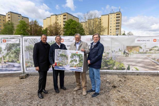 Vier Männer stehen auf einer Baustelle vor Plakaten mit Architekturentwürfen und halten gemeinsam eine Visualisierung eines Bauprojekts.