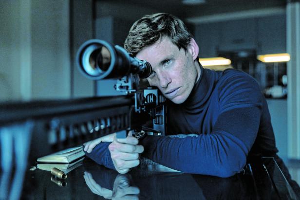 Ein Mann zielt konzentriert mit einem Scharfschützengewehr durch ein Zielfernrohr in einem dunklen Raum.