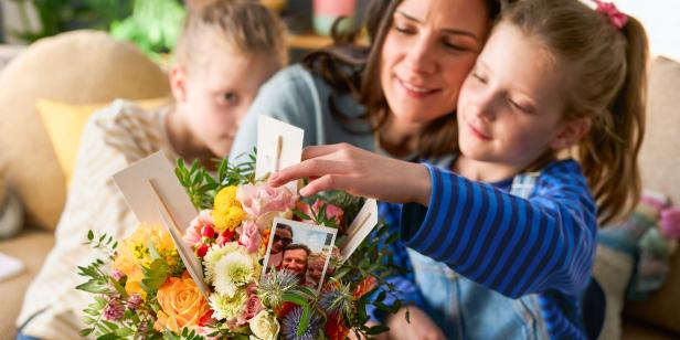 Ein Sohn, eine Tochter und eine Mutter an einem Blumenstrauß mit Bildern dran 