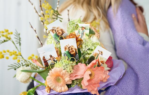 Bunter Blumenstrauß mit eingesteckten Sofortfotos, im Hintergrund eine Umarmung zweier Frauen.