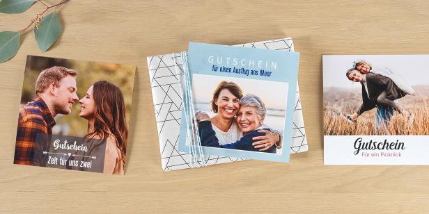Drei personalisierte Gutscheinkarten mit Fotos und Aufschriften auf einem Holztisch nebeneinander.