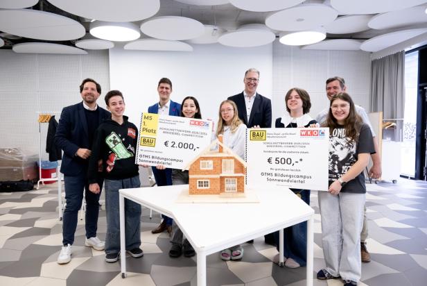 Schüler:innen und Erwachsene stehen da mit zwei Gutscheinen vor einem Rohbau auf einem Tisch. 