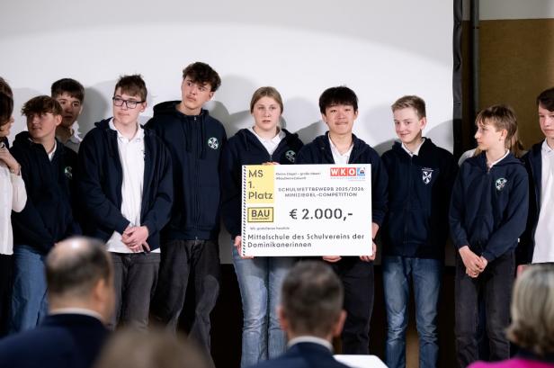 Schülergruppe hält einen großen Scheck für den ersten Platz beim Miniziegel-Wettbewerb.