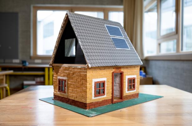 Modellhaus aus Miniziegeln mit Solarpaneelen auf dem Dach auf einem Tisch im Klassenraum.