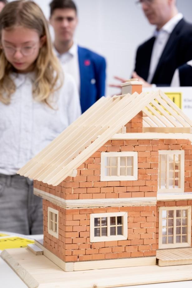 Ein detailreiches Miniaturhaus aus Ziegelsteinen steht vor mehreren Personen.