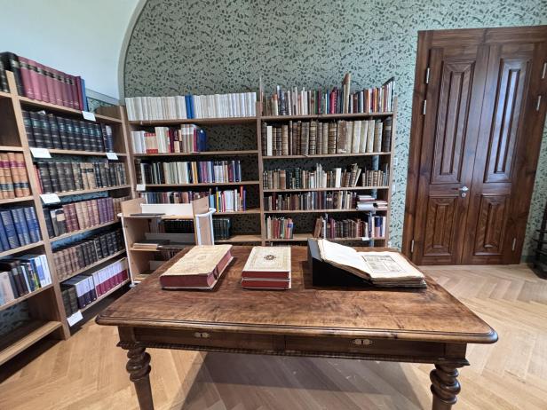 Historische Bibliothek mit alten Büchern in Regalen und auf einem Holztisch vor Holztür.