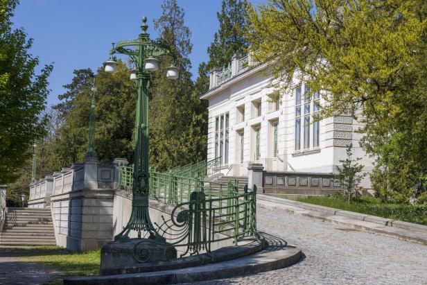 Grünes schmiedeeisernes Geländer und Laternen führen eine steinerne Rampe zu einem weißen Gebäude mit großen Fenstern hinauf.