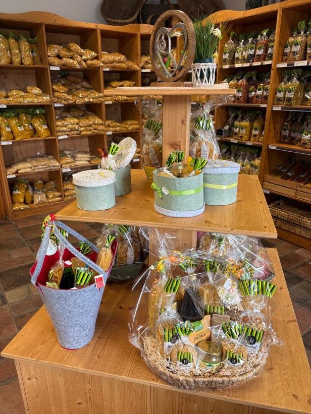 Geschenksets mit verschiedenen Lebensmitteln und Nudeln stehen auf Holztischen in einem Laden mit vollen Regalen im Hintergrund.