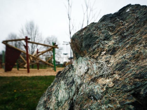 Großer Felsen im Vordergrund, im Hintergrund ein unscharfer Spielplatz mit Klettergerüst und Bäumen.