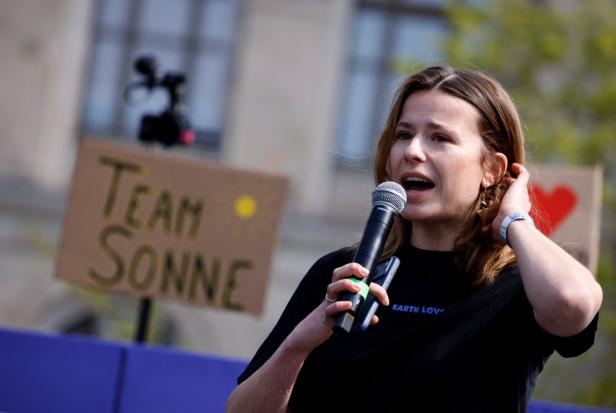 Luisa Neubauer spricht ins Mikrofon vor Schildern mit Aufschriften wie "Team Sonne".