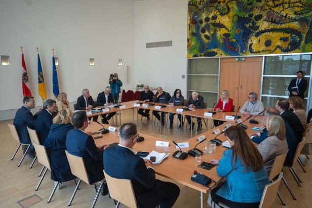 Mehrere Personen sitzen an einem großen Konferenztisch in einem modernen Raum mit Flaggen und bunter Wandkunst.