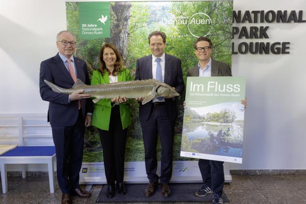Vier Personen präsentieren bei der Jubiläumsveranstaltung zum 30-jährigen Bestehen des Nationalparks Donau-Auen einen großen Fisch und ein Plakat zur Ausstellung „Im Fluss“.