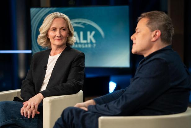 Zwei Personen diskutieren in einer TV-Talkshow vor einem Bildschirm mit "Talk im Hangar-7".