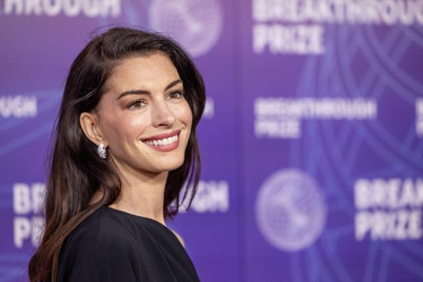 Anne Hathaway lächelt vor einem violetten "Breakthrough Prize"-Hintergrund.