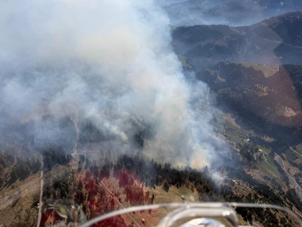 Dichter Rauch steigt von einem Waldbrand in einer bergigen Landschaft auf.