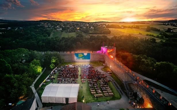 Ein Open-Air-Kino mit Publikum vor einer Burgmauer bei Sonnenuntergang.