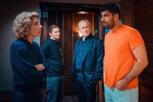 Vier Personen stehen sich in einem Raum gegenüber und blicken sich ernst an.