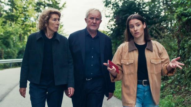 Drei Personen gehen auf einem Weg im Grünen, die Frau rechts spricht gestikulierend mit den anderen beiden.