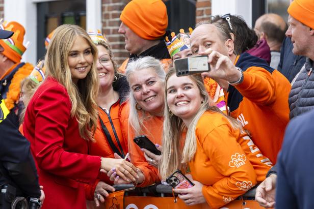 Prinzessin Amalia schüttelt Hände mit Fans, die orange Kleidung und Hüte tragen und Fotos machen.