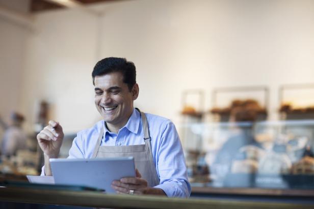 Ein lächelnder Mann mit Schürze bedient ein Tablet in einer Bäckerei.