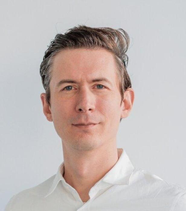 Ein Mann mit hellen Augen und weißem Hemd blickt in die Kamera.