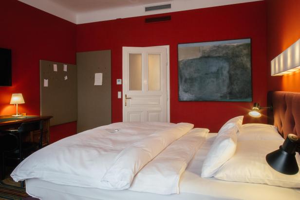 Ein Bett, dahinter ein abstraktes Bild auf roter Wand