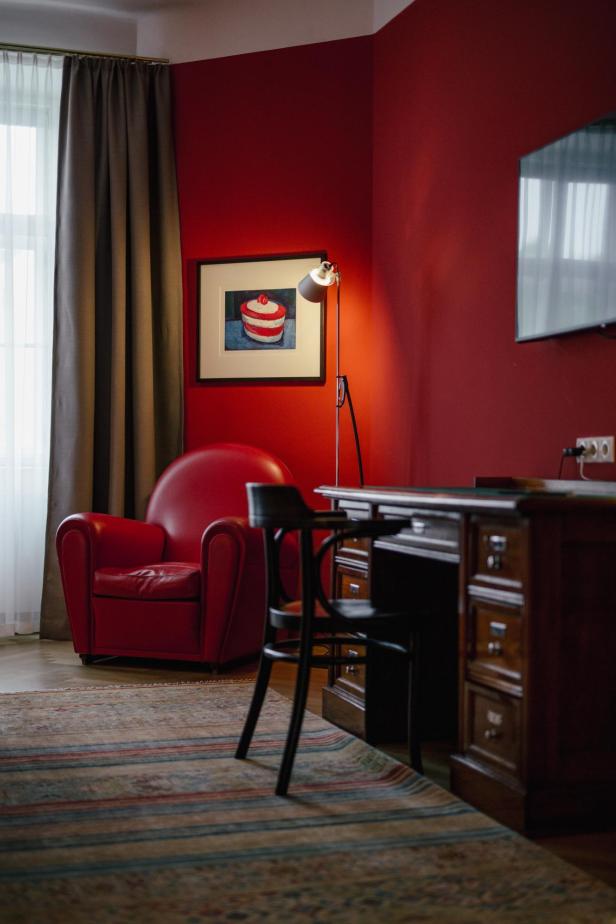 Blick in ein Hotelzimmer mit rotem Ledersessel und einem Bild mit Torte