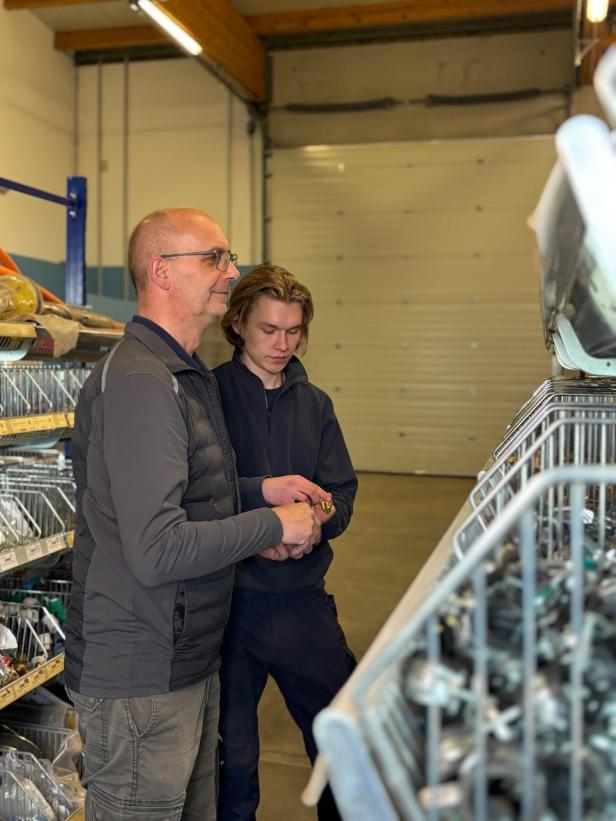 Zwei Männer stehen in einem Lager vor Regalen mit Ersatzteilen.