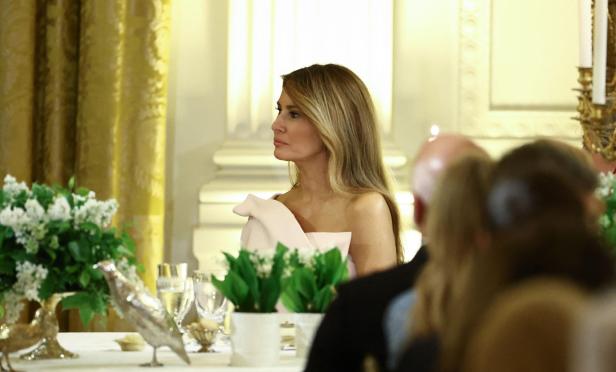 Melania Trump sitzt bei einem formellen Dinner mit Blumenschmuck und goldenen Akzenten.