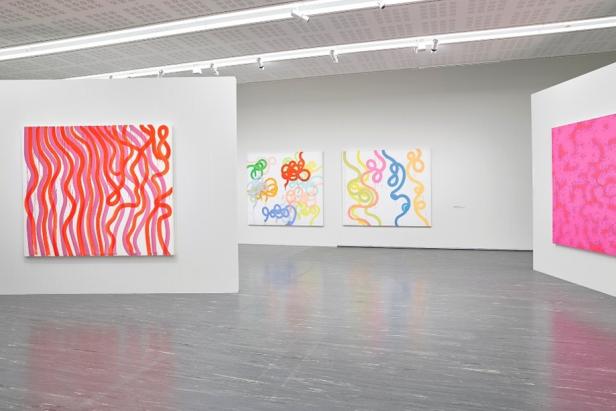 Mehrere abstrakte Gemälde mit bunten, geschwungenen Linien und Mustern hängen in einem modernen Ausstellungsraum.