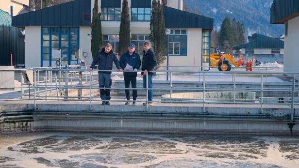 Drei Männer stehen an einem Becken der Kläranlage und betrachten ein Dokument.
