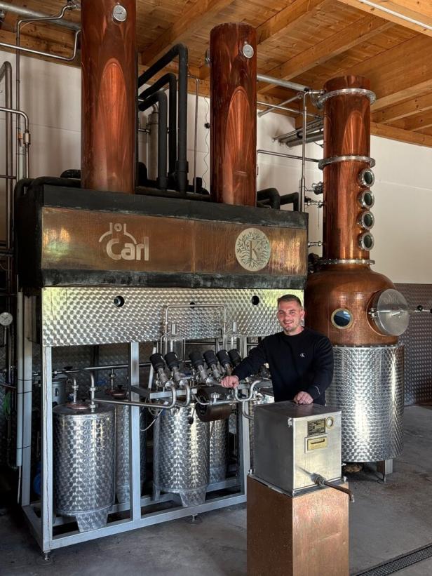 Ein Mann steht vor einer großen Destillationsanlage aus Kupfer und Edelstahl in einer Brennerei.