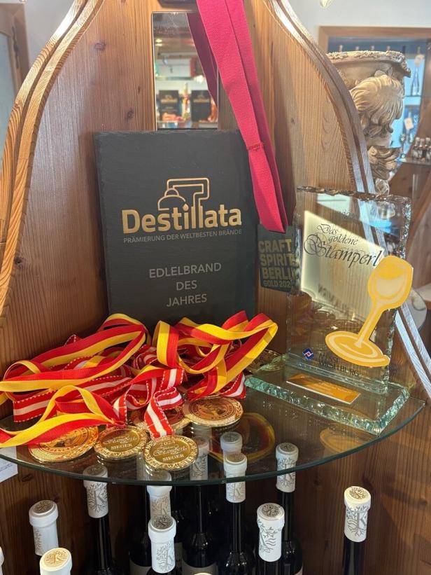 Mehrere Medaillen, Auszeichnungen und Flaschen stehen auf einem Holzregal, darunter eine Trophäe und ein Destillata-Preis.