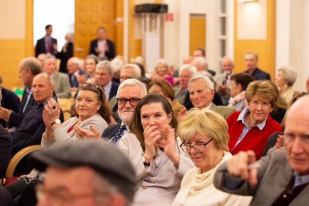Viele Menschen sitzen in einem Publikum und applaudieren.