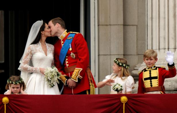 Auf einem Balkon küssen sich Kate und William, flankiert von Blumenmädchen und einem Pagen in Uniform.