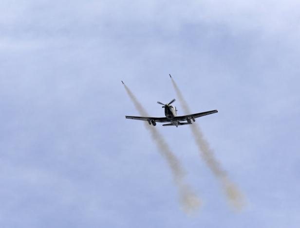 Ein Propellerflugzeug feuert zwei Raketen ab, die Rauchspuren am Himmel hinterlassen.